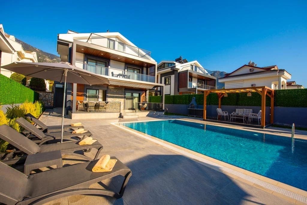 Gündüz vakti havuz başı şezlonglar ve şemsiyeler bulunan çok katlı lüks villa dış cephesi.