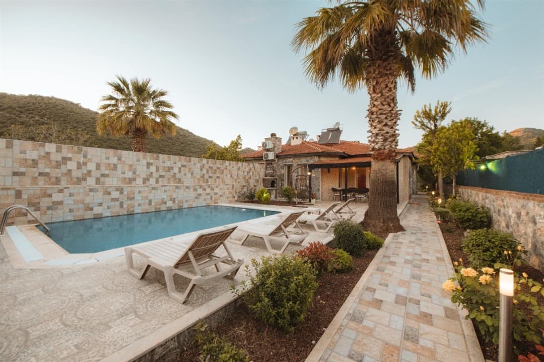 Palm ağaçları ve şezlongların bulunduğu havuzlu taş villa bahçesi.