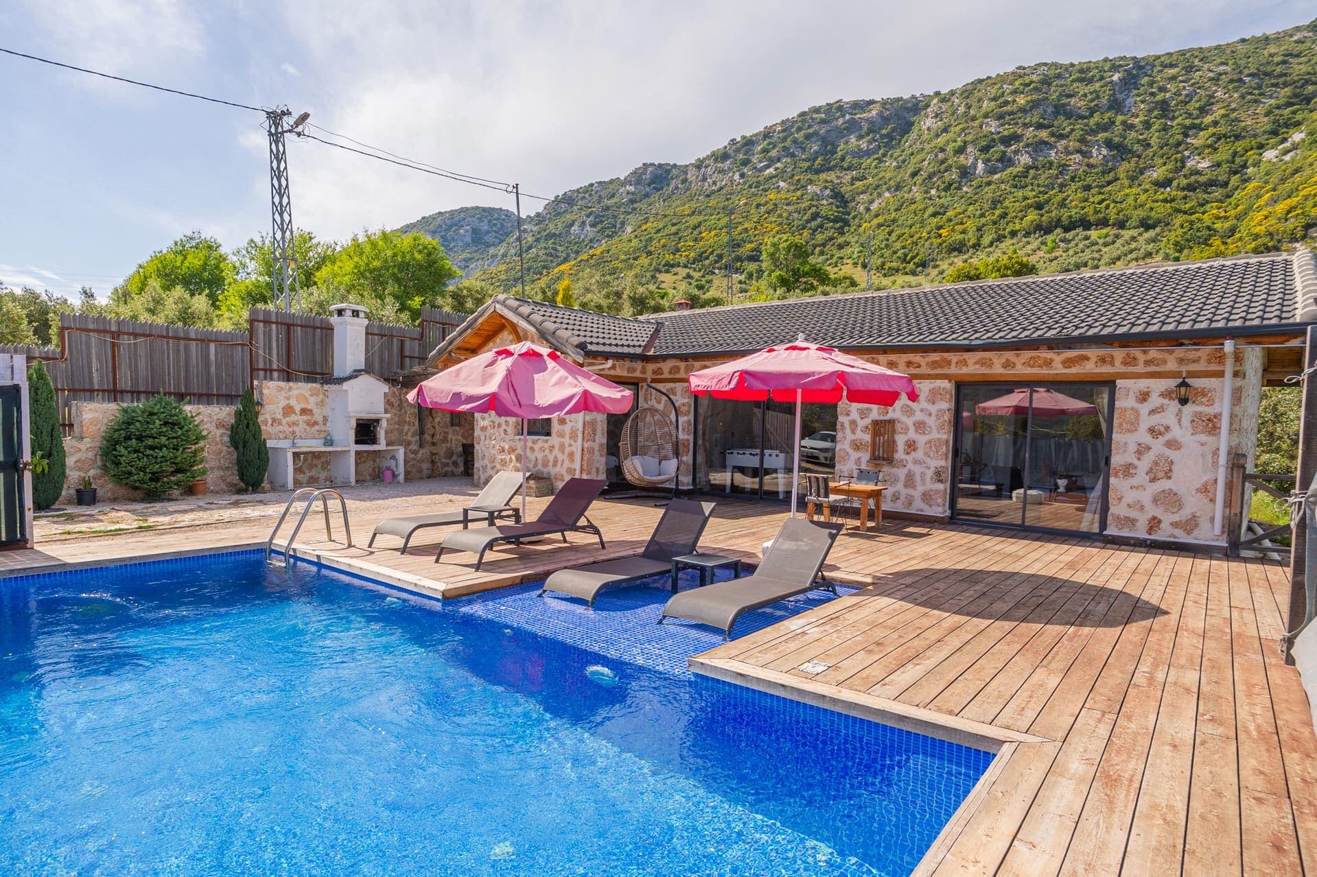 Dağ manzaralı havuz kenarında şezlonglar ve şemsiyeler bulunan villa bahçesi.