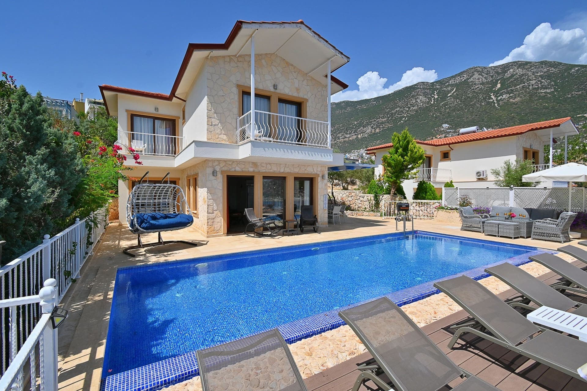 Dağ eteklerinde, havuzlu ve iki katlı taş detaylı villa dış cephesi.