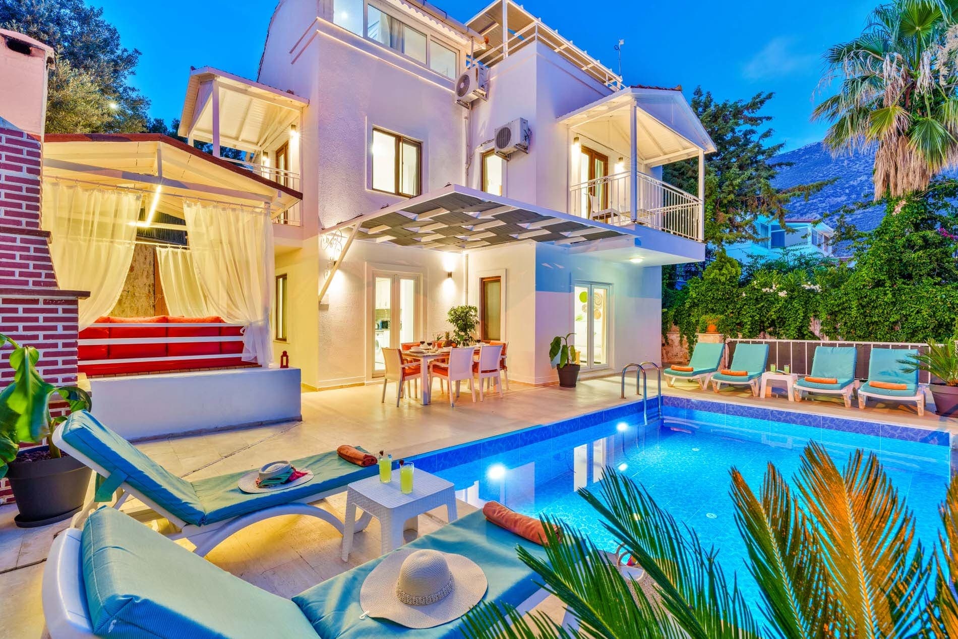 Akşam aydınlatmalı havuz kenarında şezlonglar ve iki katlı beyaz villa.