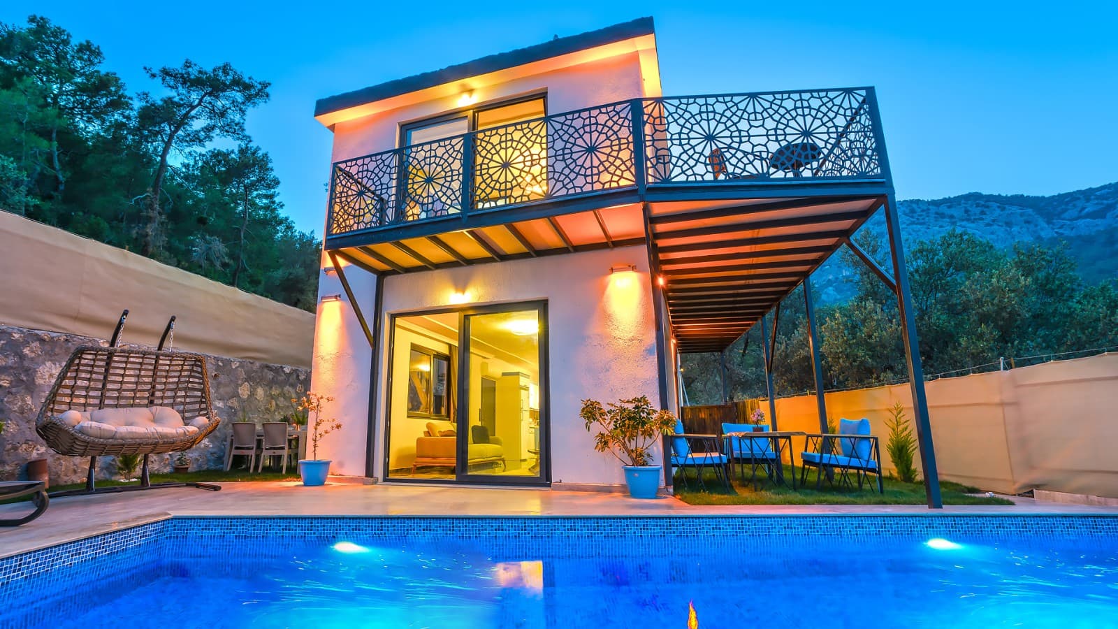 Akşam aydınlatmalı iki katlı taş villa ve önündeki havuz.