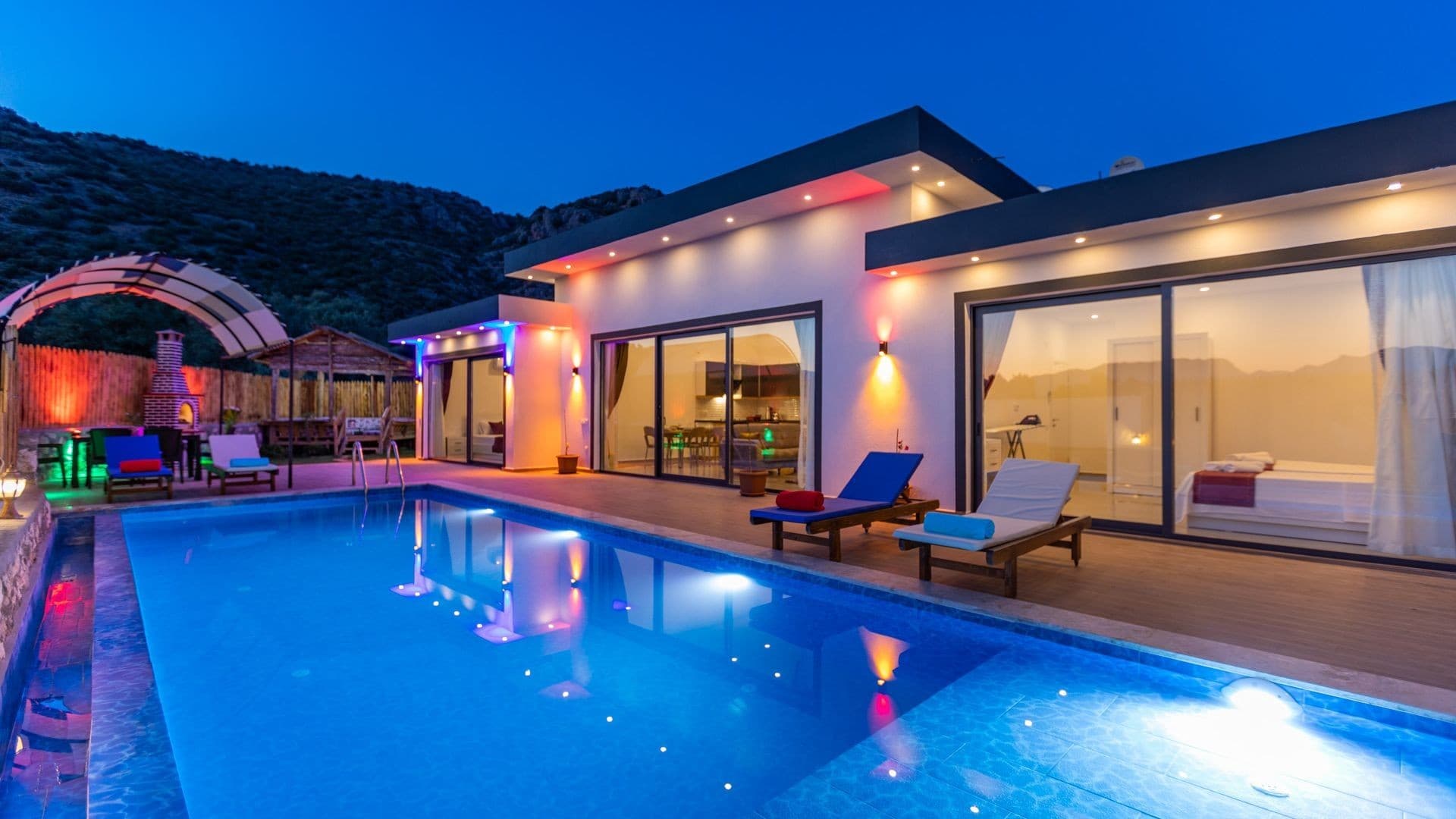 Akşam vakti havuz başı aydınlatmalı, şezlonglu tek katlı modern villa.