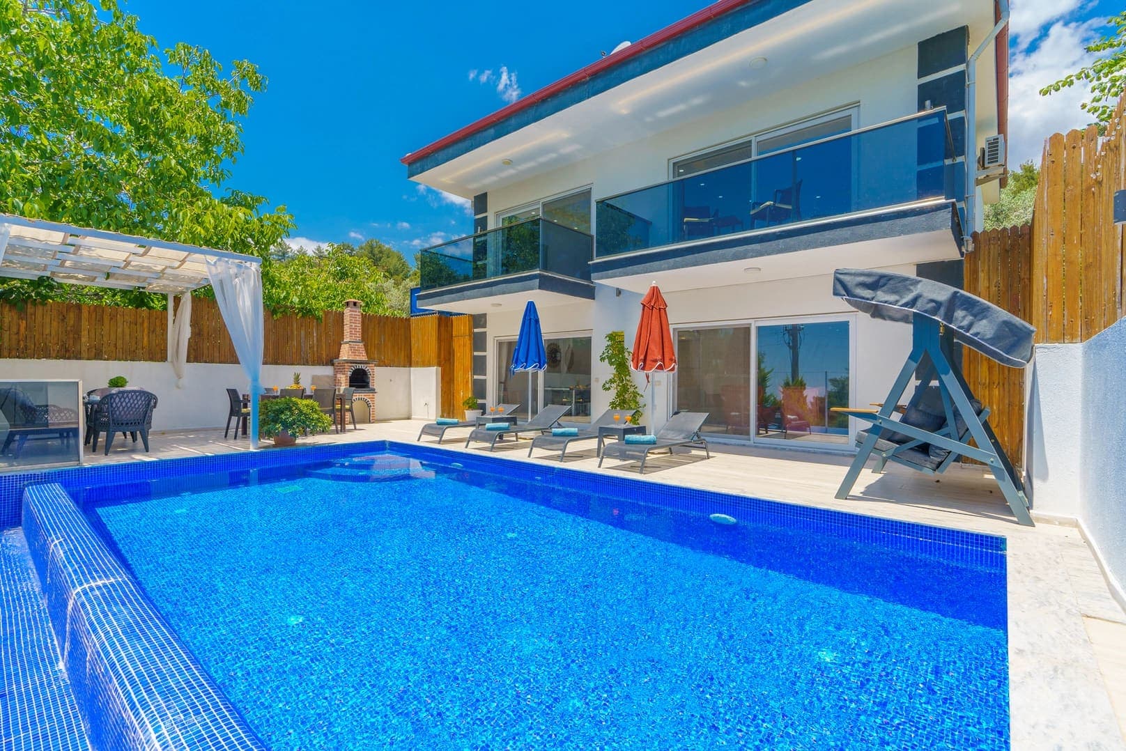 Bahçesinde havuz, şezlonglar ve salıncak bulunan iki katlı villa.