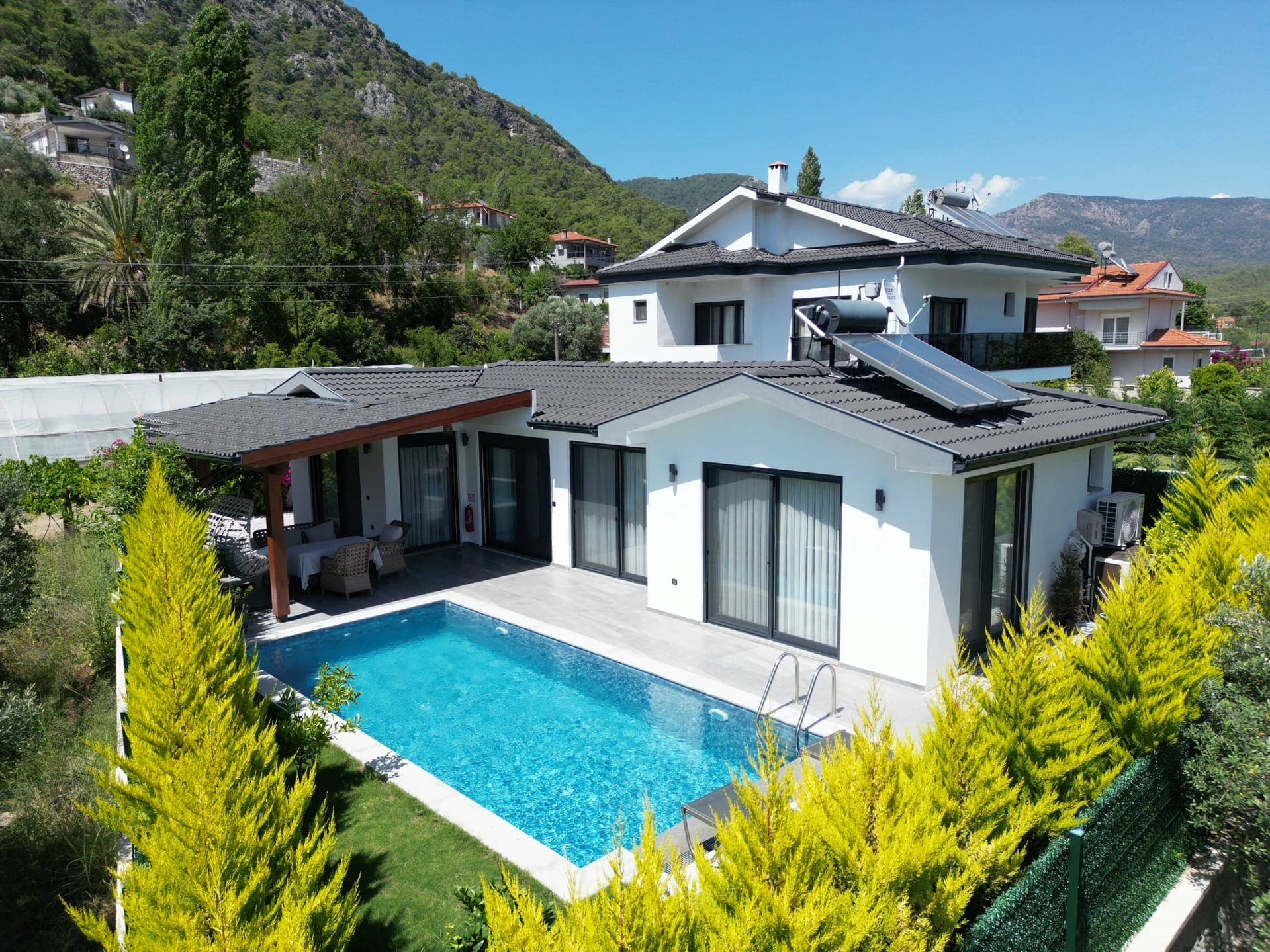 Ağaçlar arasında havuzlu ve verandalı beyaz villa.