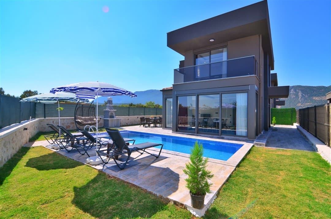 Önünde özel havuzu, şezlongları ve bahçesi bulunan modern iki katlı villa.