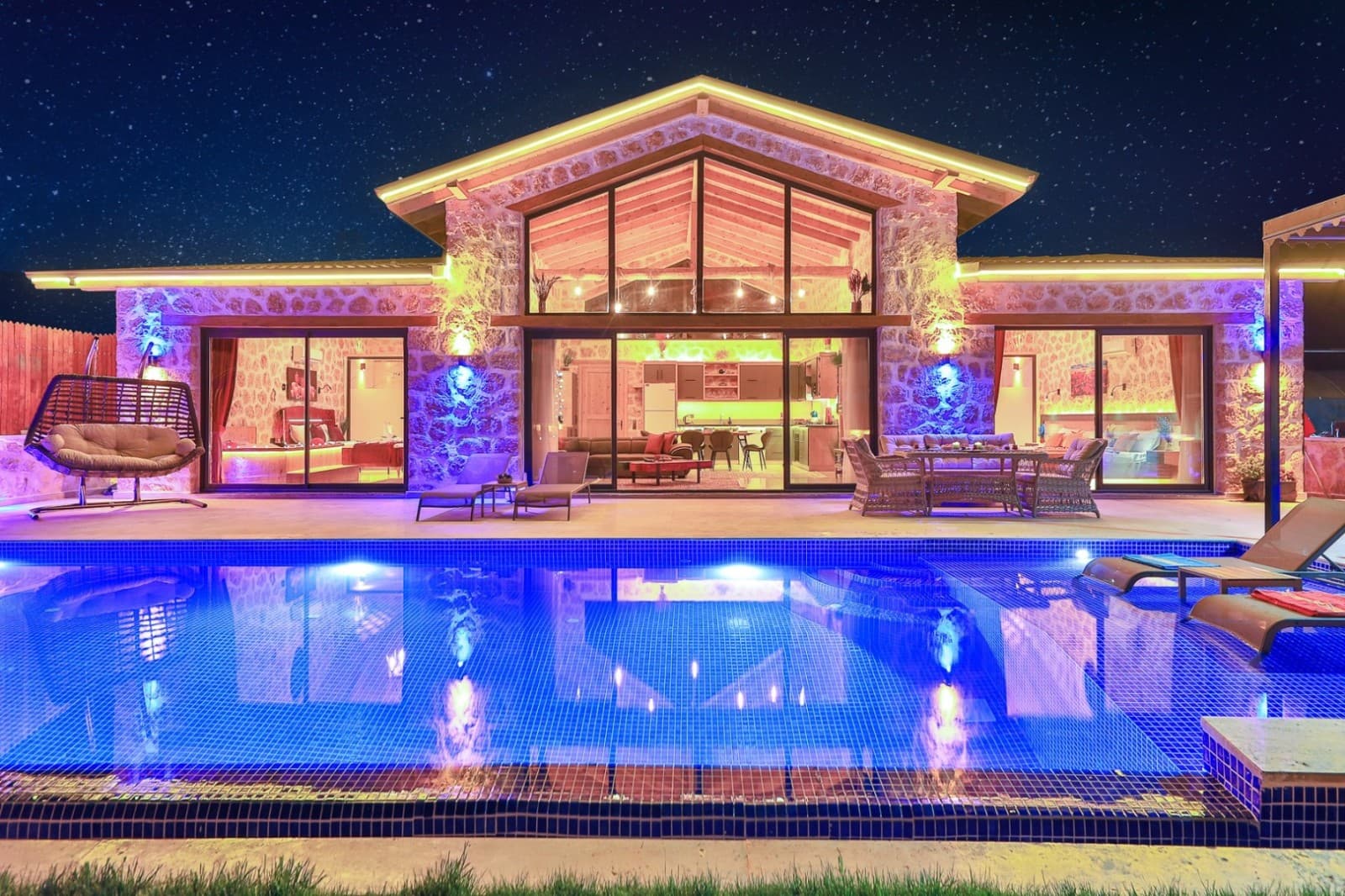 Gece aydınlatmalı taş villanın önünde havuz ve bahçe oturma alanı.