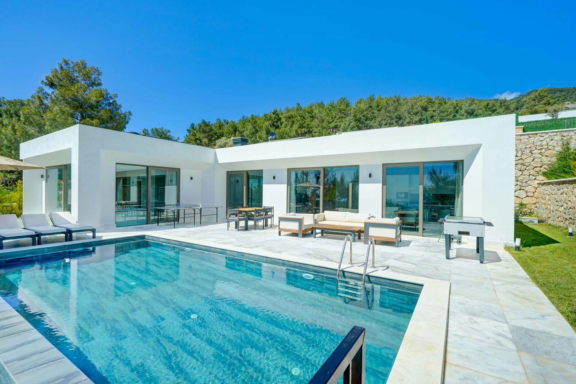 Beyaz cepheli, havuzlu ve şezlonglu terası bulunan tek katlı modern villa.