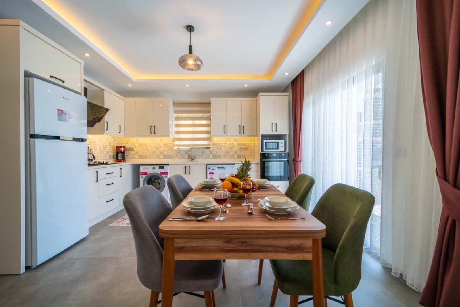 Ahşap yemek masası, sandalyeler ve arka planda beyaz mutfak dolapları