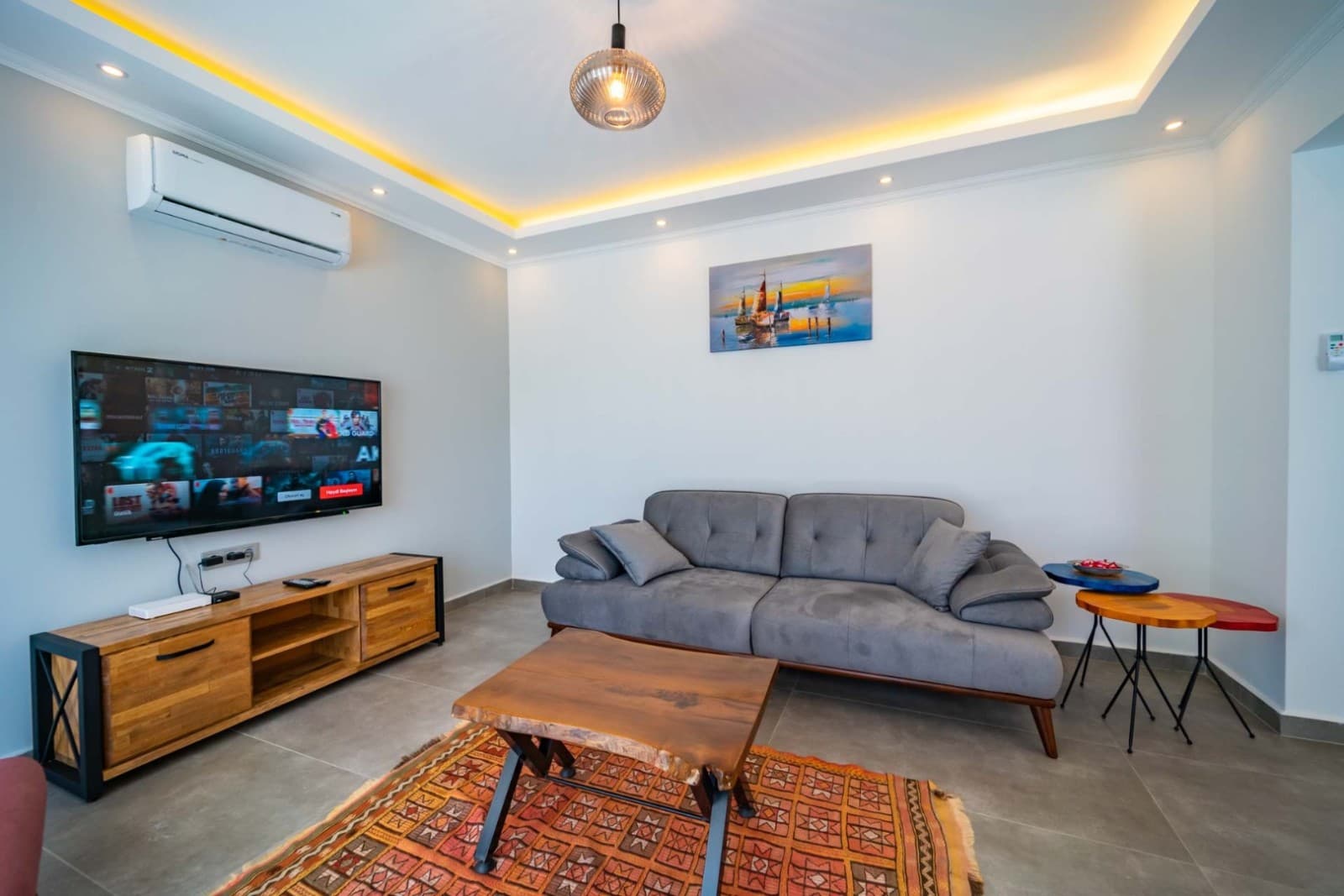 Gri kanepe, ahşap sehpalar ve televizyon bulunan oturma odası.