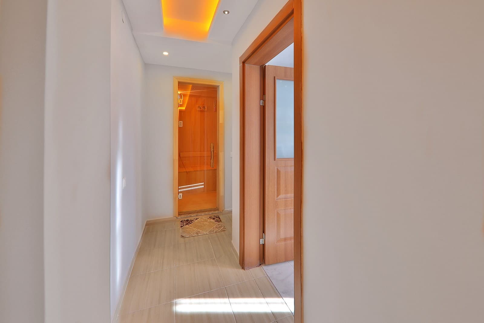 Aydınlatmalı koridorun sonunda ahşap kaplı sauna odası kapısı.