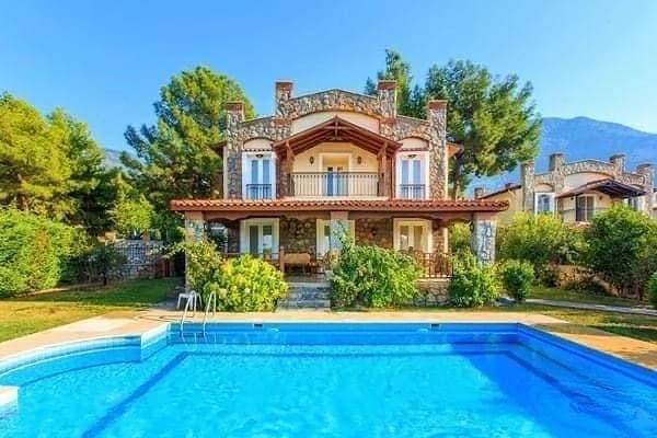 Taş detaylı iki katlı villanın önündeki havuzun ve bahçenin görünümü