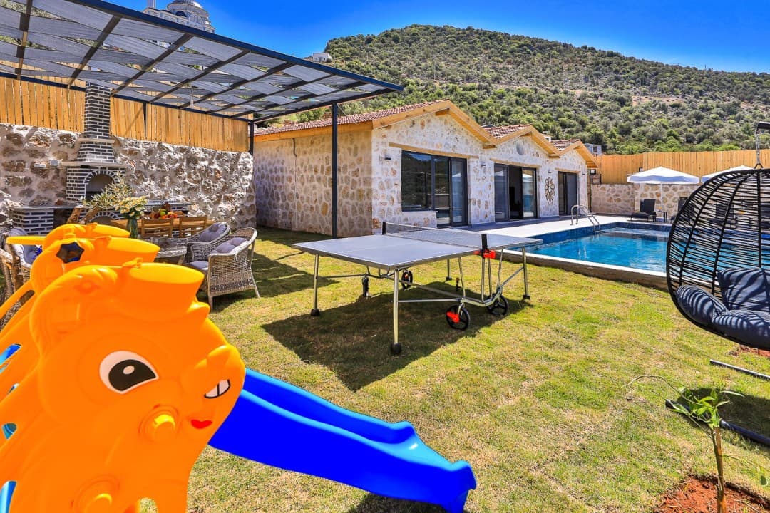 Taş villanın havuzlu bahçesinde masa tenisi, salıncak ve çocuk kaydırağı var.