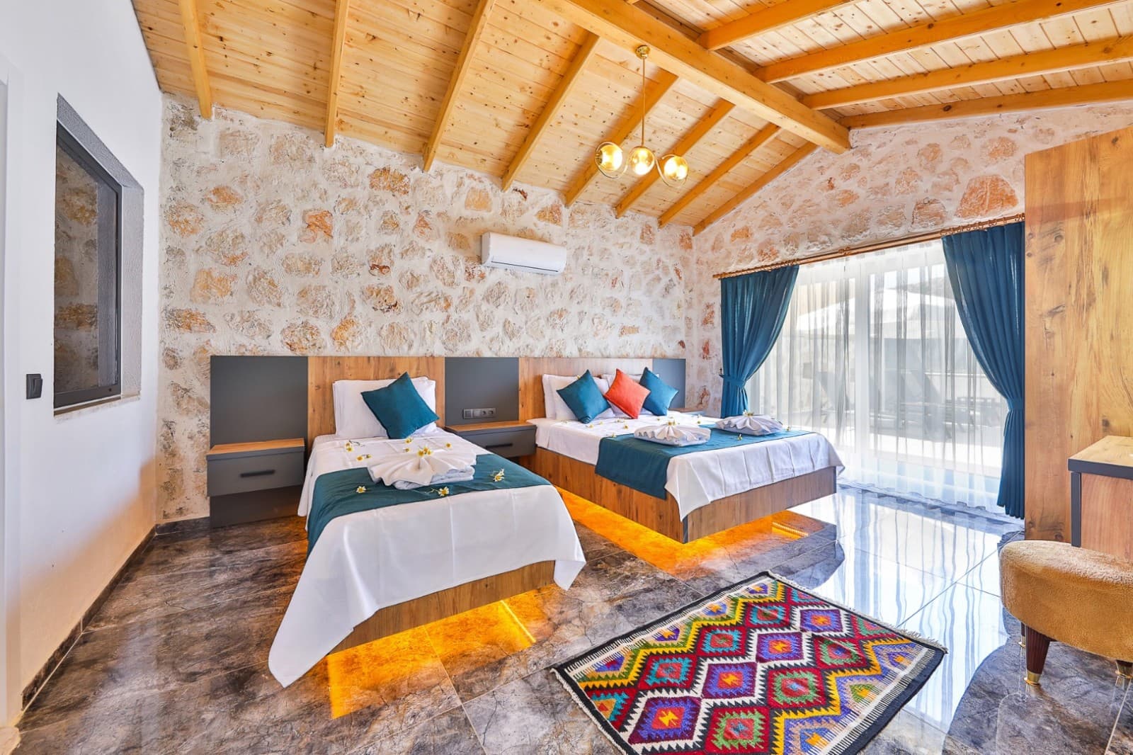 Taş duvarlı odada iki yatak, renkli yastıklar ve kilim