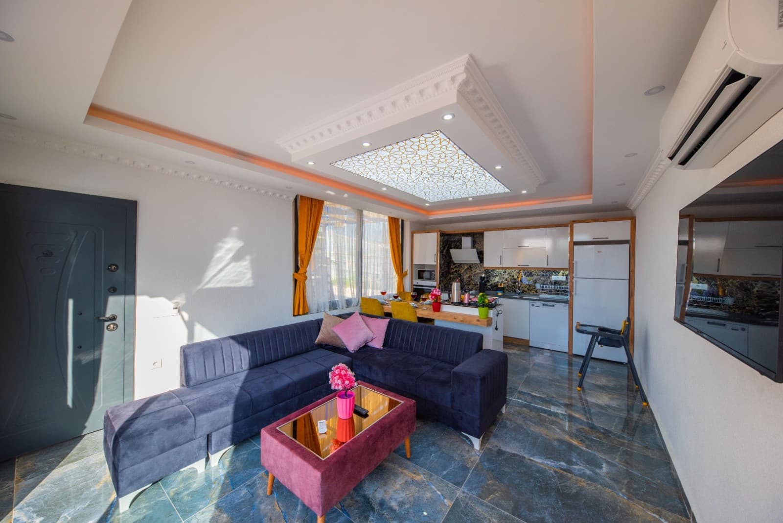 Lacivert köşe koltuk ve açık mutfağın yer aldığı salon.