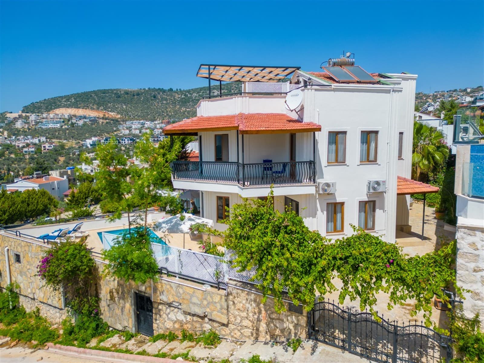Bahçesinde havuz ve şezlonglar bulunan beyaz dış cepheli iki katlı villa.