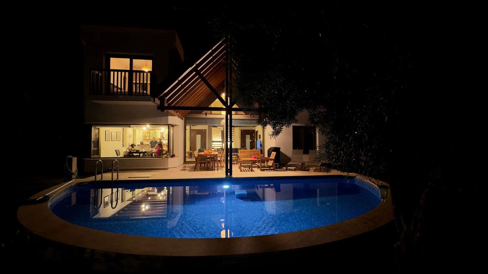 Gece aydınlatmalı havuz ve arka planda ışıkları yanan villa.