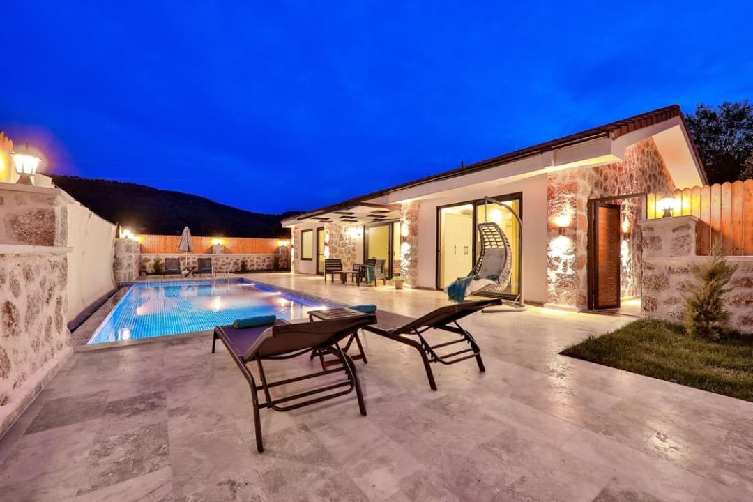 Akşam saatlerinde taş duvarlı, havuzlu ve şezlonglu villa bahçesi.