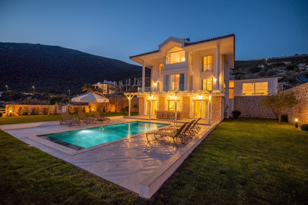Akşam vakti aydınlatılmış, havuzlu ve bahçeli üç katlı müstakil villa.