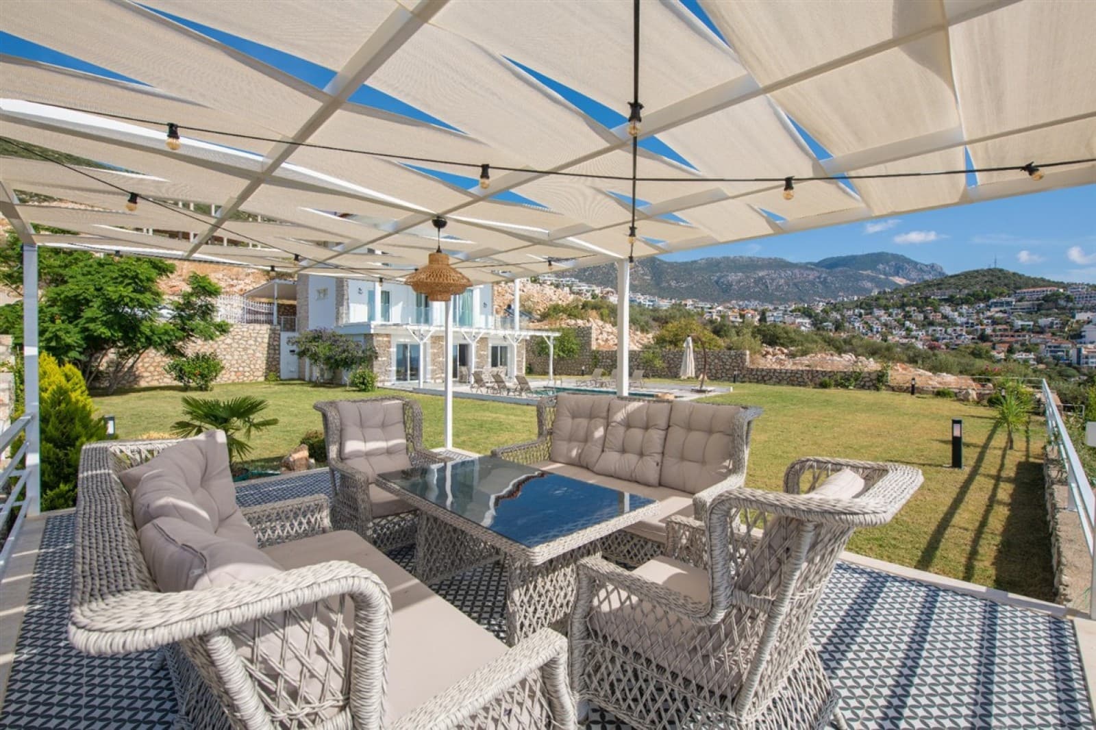 Güneşlikli pergola altında gri hasır oturma grubu ve yemek masası olan geniş bahçe ve teras.
