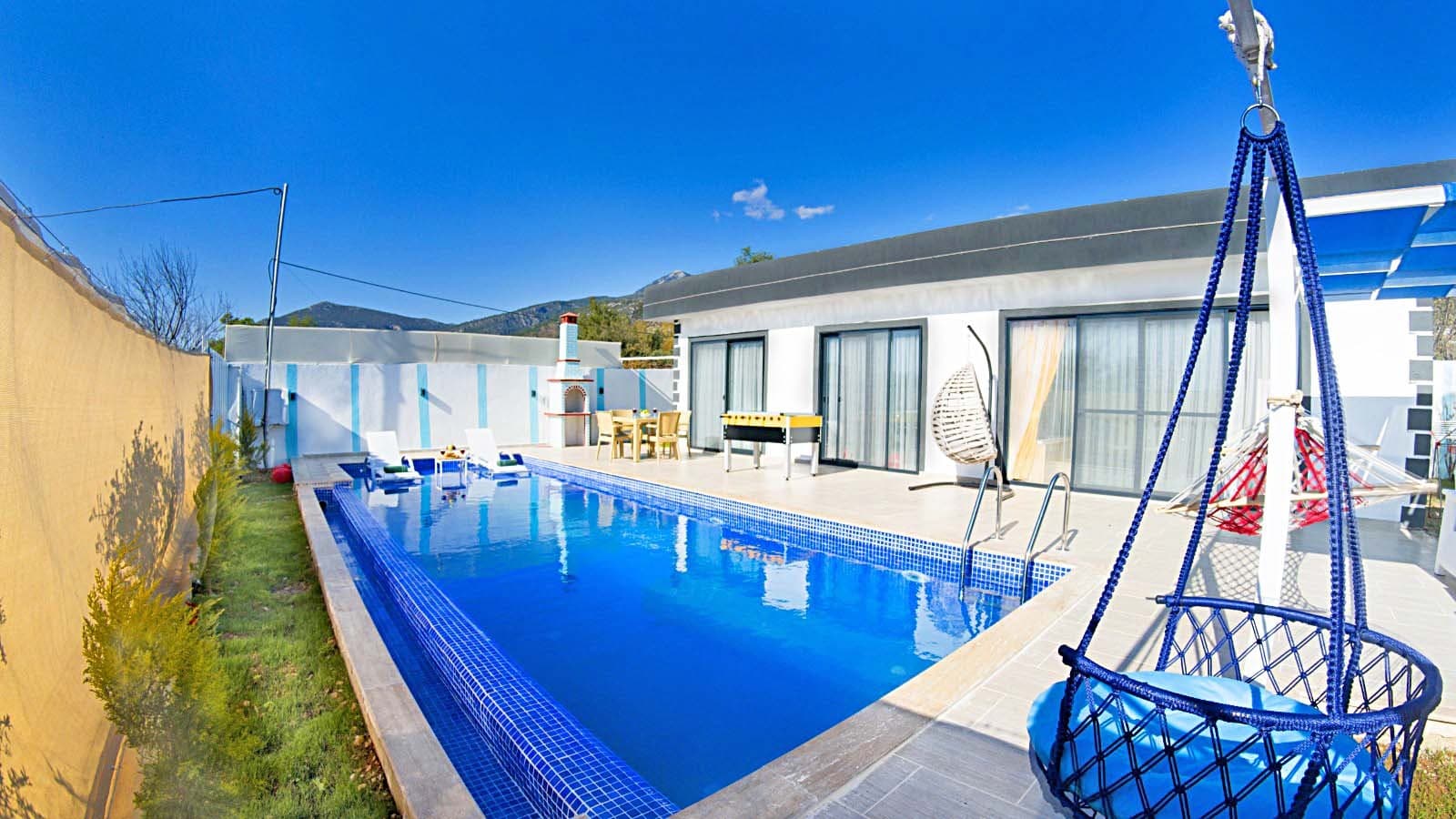 Mavi havuzlu, şezlonglu ve salıncaklı villa terası.