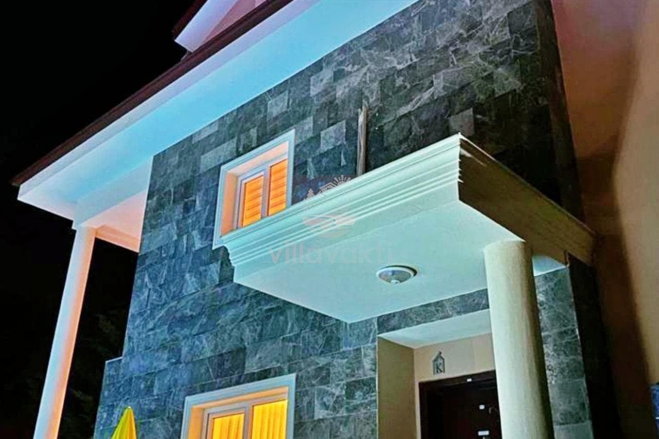 Gri taş kaplı dış cephesi ve balkonu olan villanın gece çekimi.
