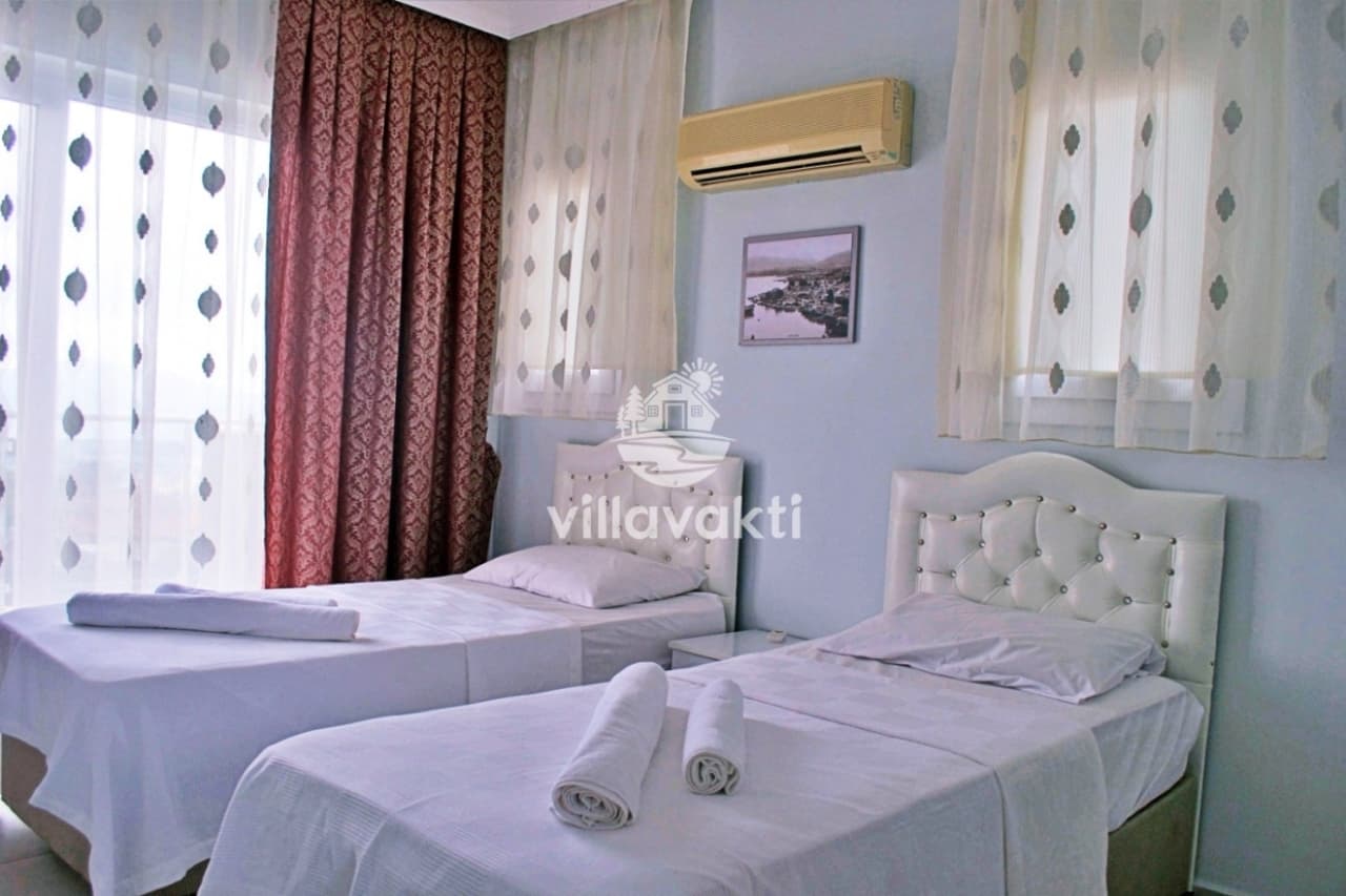 Beyaz başlıklı iki tek kişilik yatak ve perdeli pencere bulunan yatak odası.
