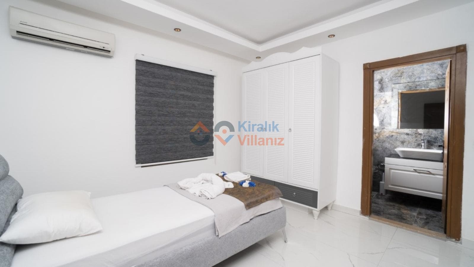 Tek kişilik yatak, gardırop ve açık banyo kapısı görünen yatak odası.
