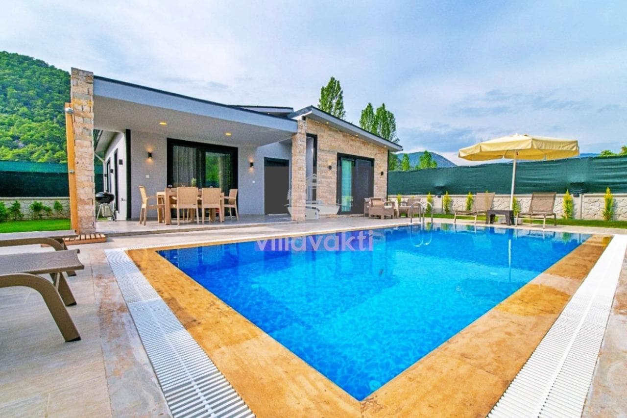 Tek katlı taş detaylı villanın önündeki havuz ve veranda alanı.