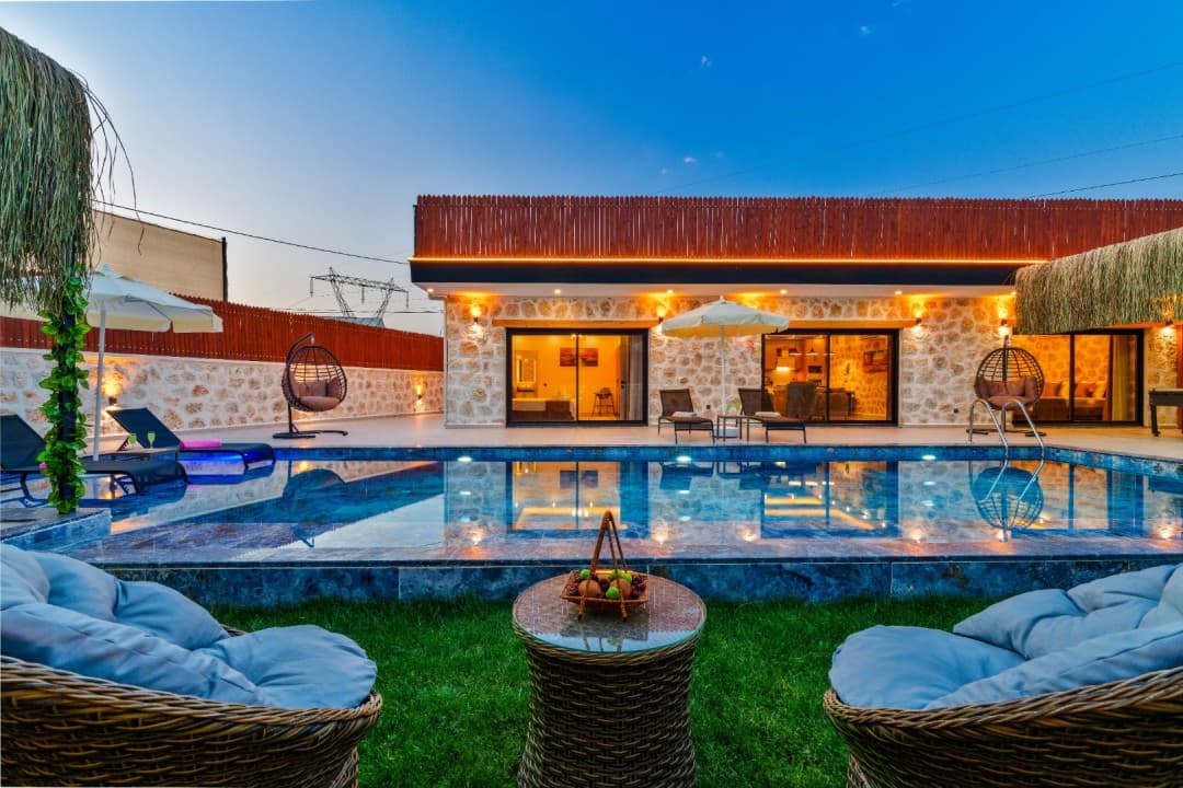 Akşam vakti aydınlatmalı havuz başında salıncak ve şezlonglar bulunan taş villa.