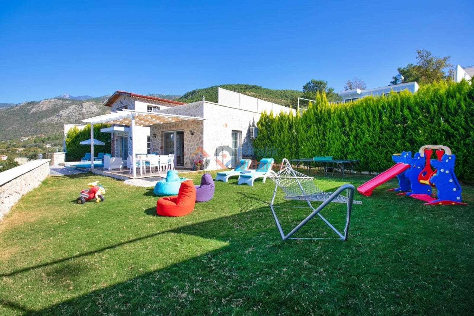 Geniş çim bahçesinde çocuk oyun parkı olan taş villa.