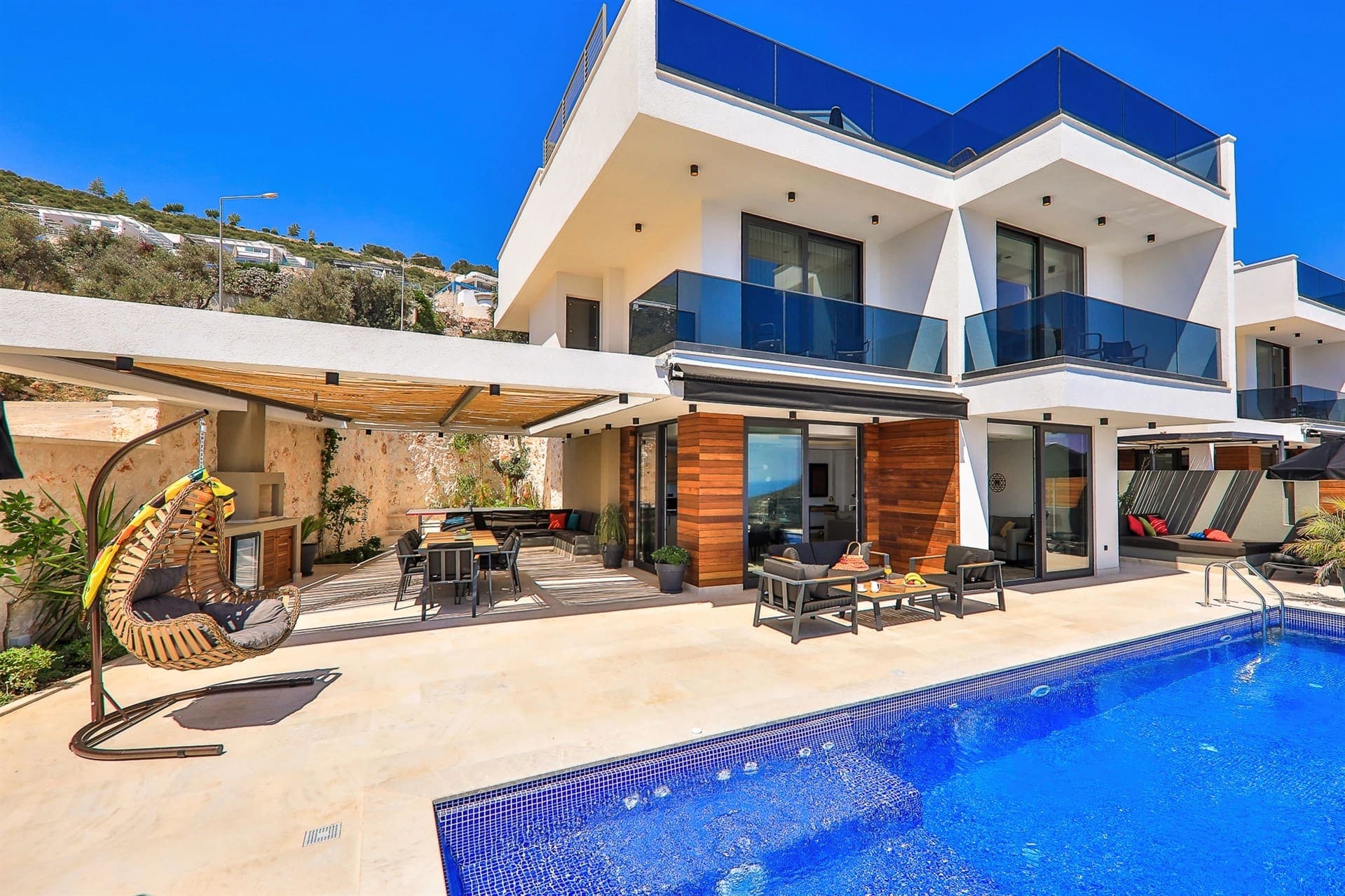 Havuz kenarında oturma grubu ve salıncak bulunan modern villa cephesi.