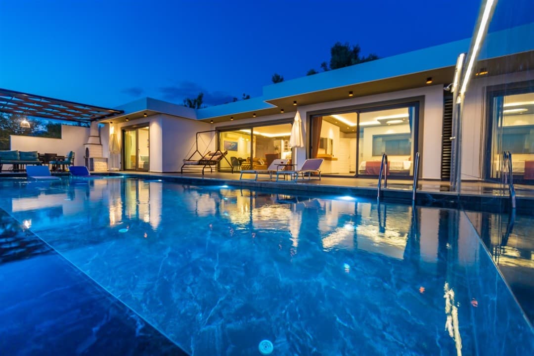Aydınlatmalı yüzme havuzu ve şezlongların yer aldığı modern tek katlı villa.