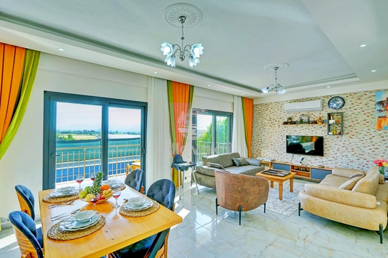 Manzaralı pencerelerin önünde yemek masası ve oturma grubu bulunan salon.