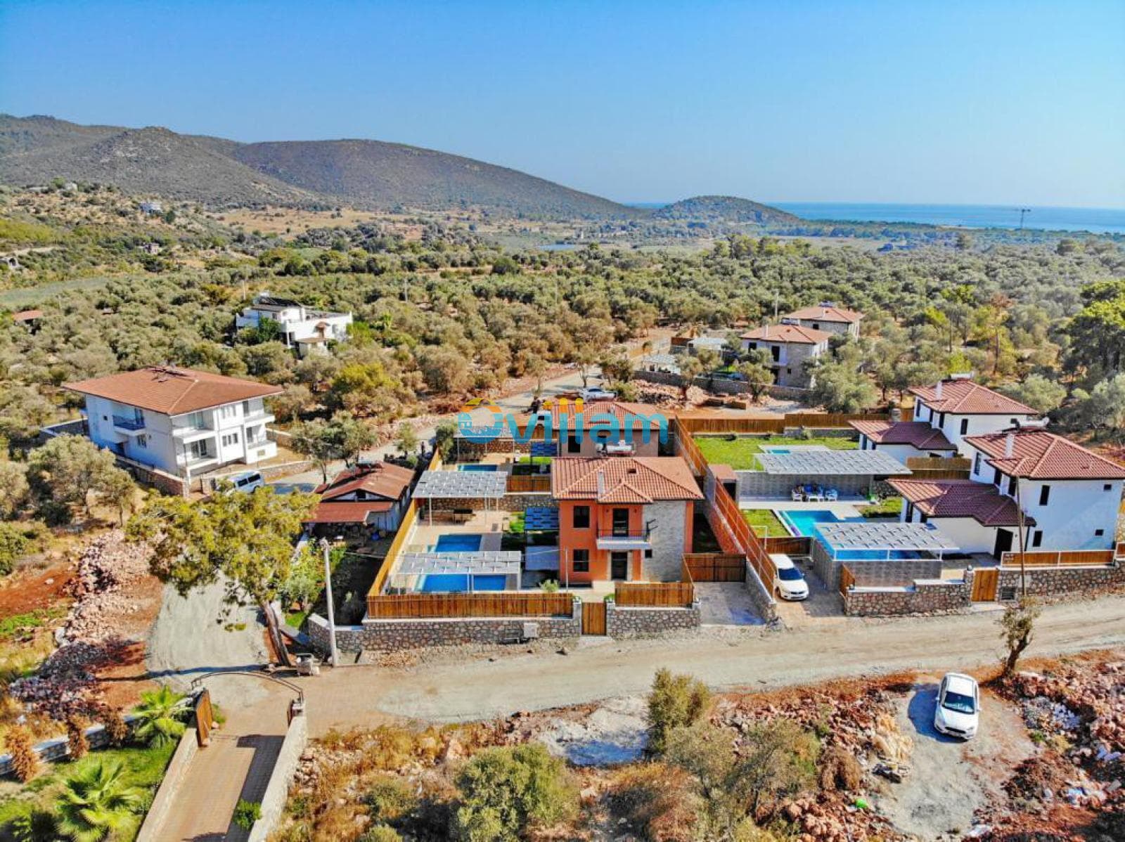 Ağaçlar ve dağlarla çevrili alandaki villaların kuşbakışı görünümü.