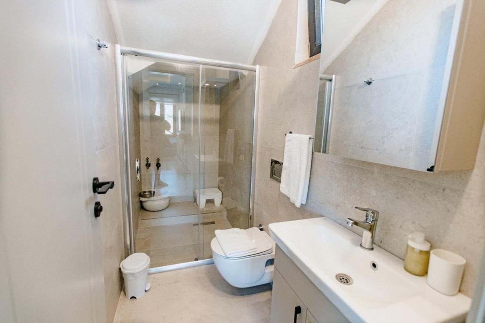 Gri tonlarında fayanslara sahip banyo, duşakabin ve lavabo.