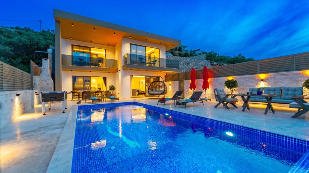 Akşam saatlerinde aydınlatmalı havuzu ve şezlongları olan modern iki katlı villa.