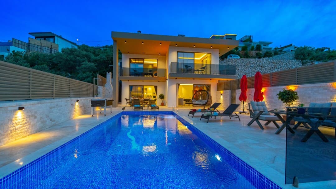 Akşam vakti havuz başı aydınlatmalı, iki katlı modern villanın dış görünümü.