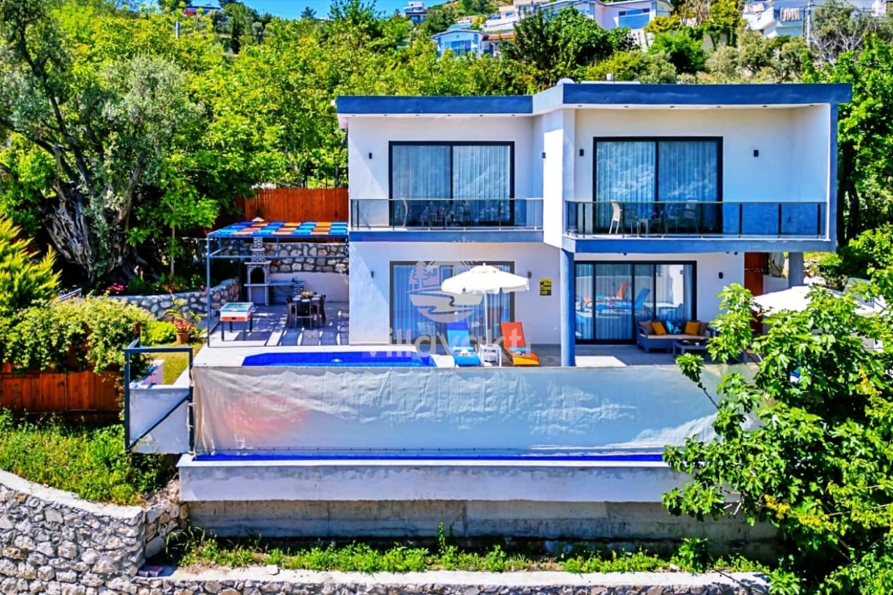 İki katlı beyaz villa önünde havuz ve bahçe.