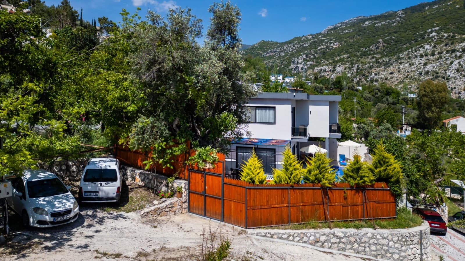 Yeşillikler ve dağ manzarası içinde, önünde otoparkı bulunan iki katlı beyaz villa.