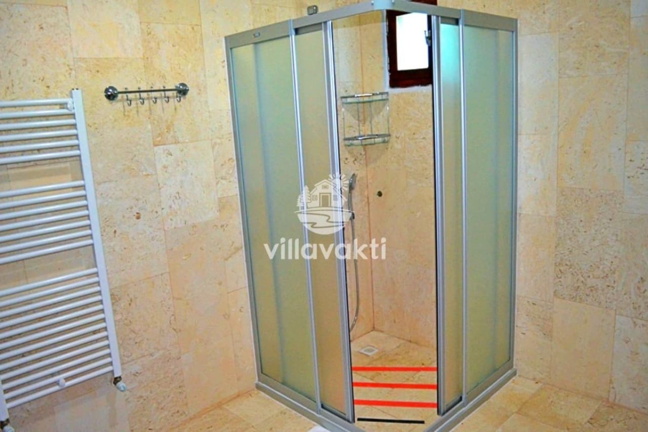 Bej seramik kaplı duşakabin ve duş başlığı bulunan banyo.