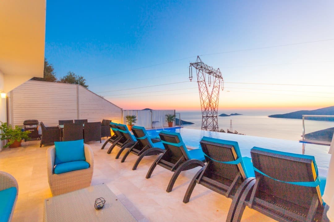 Gün batımında sonsuzluk havuzu ve şezlongların bulunduğu villa terası.