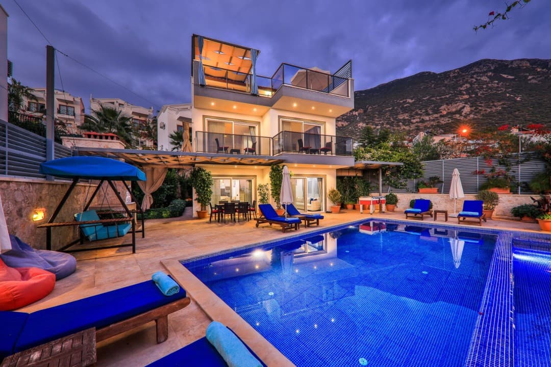 Alacakaranlıkta aydınlatılmış havuz ve bahçesinde salıncak olan villa.