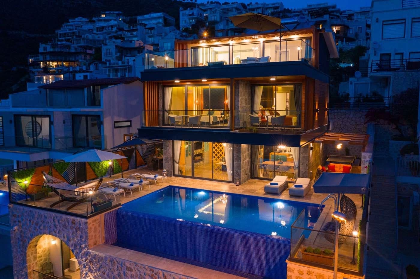 Akşam saatlerinde aydınlatılmış, havuzlu ve balkonlu modern dış cephe.