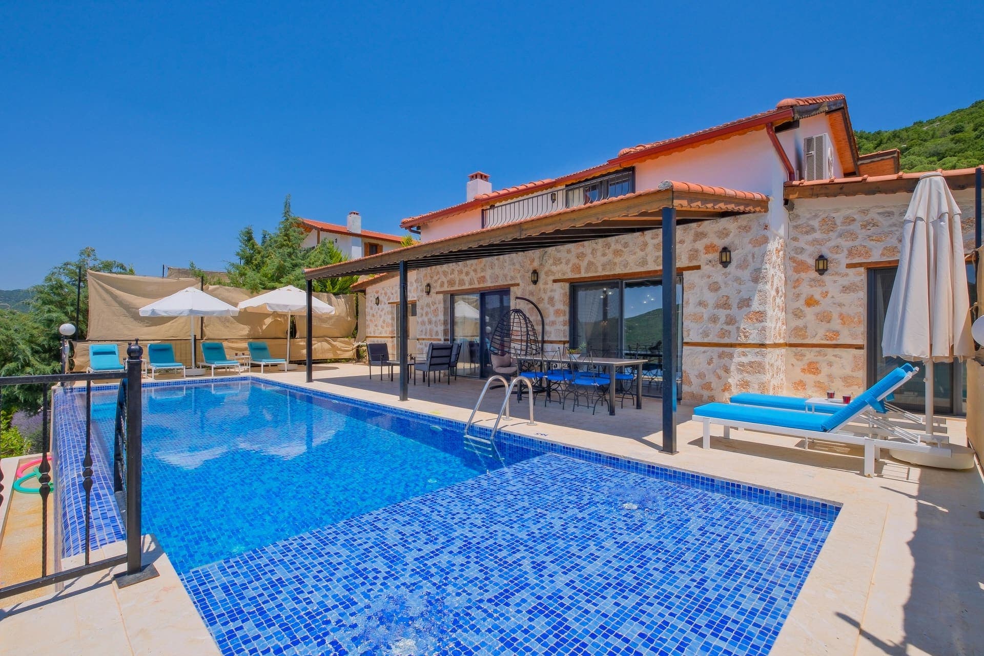 Mavi şezlongların bulunduğu havuz kenarı ve arkasında villa dış cephesi.