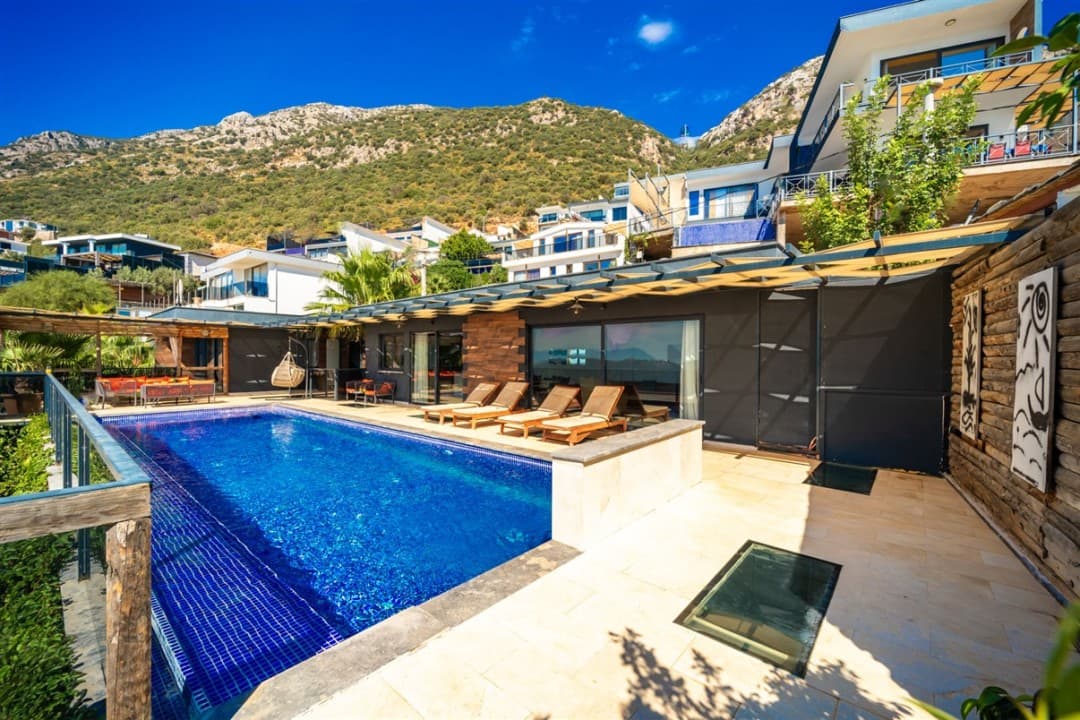 Dağ yamacında, özel havuzlu, güneşlenme şezlongları bulunan modern bir villa terası.