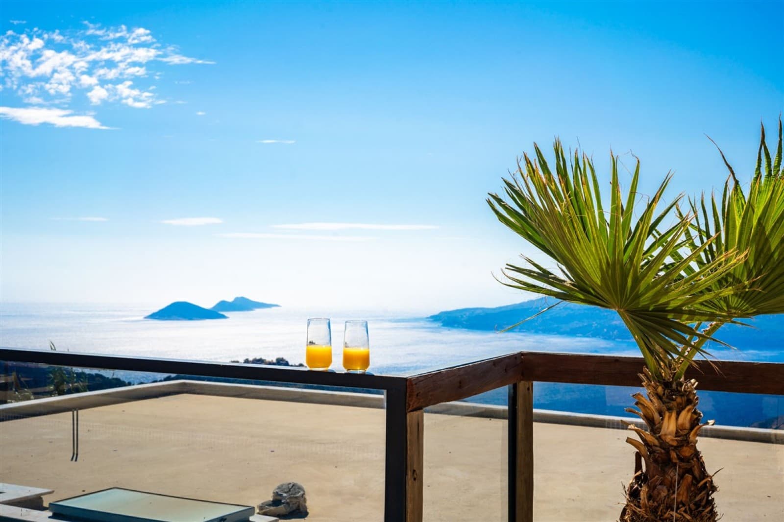 Balkon korkuluğunda iki bardak meyve suyu ve deniz manzarası.