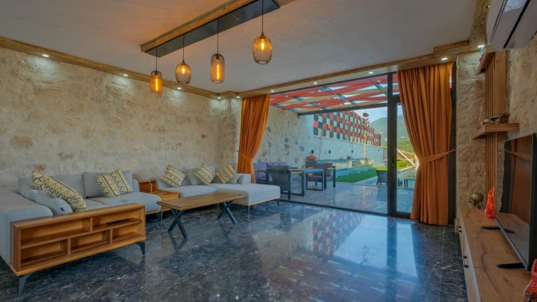Taş duvarlı, gri köşe koltuklu, ahşap orta sehpalı ve teras manzaralı modern oturma odası.