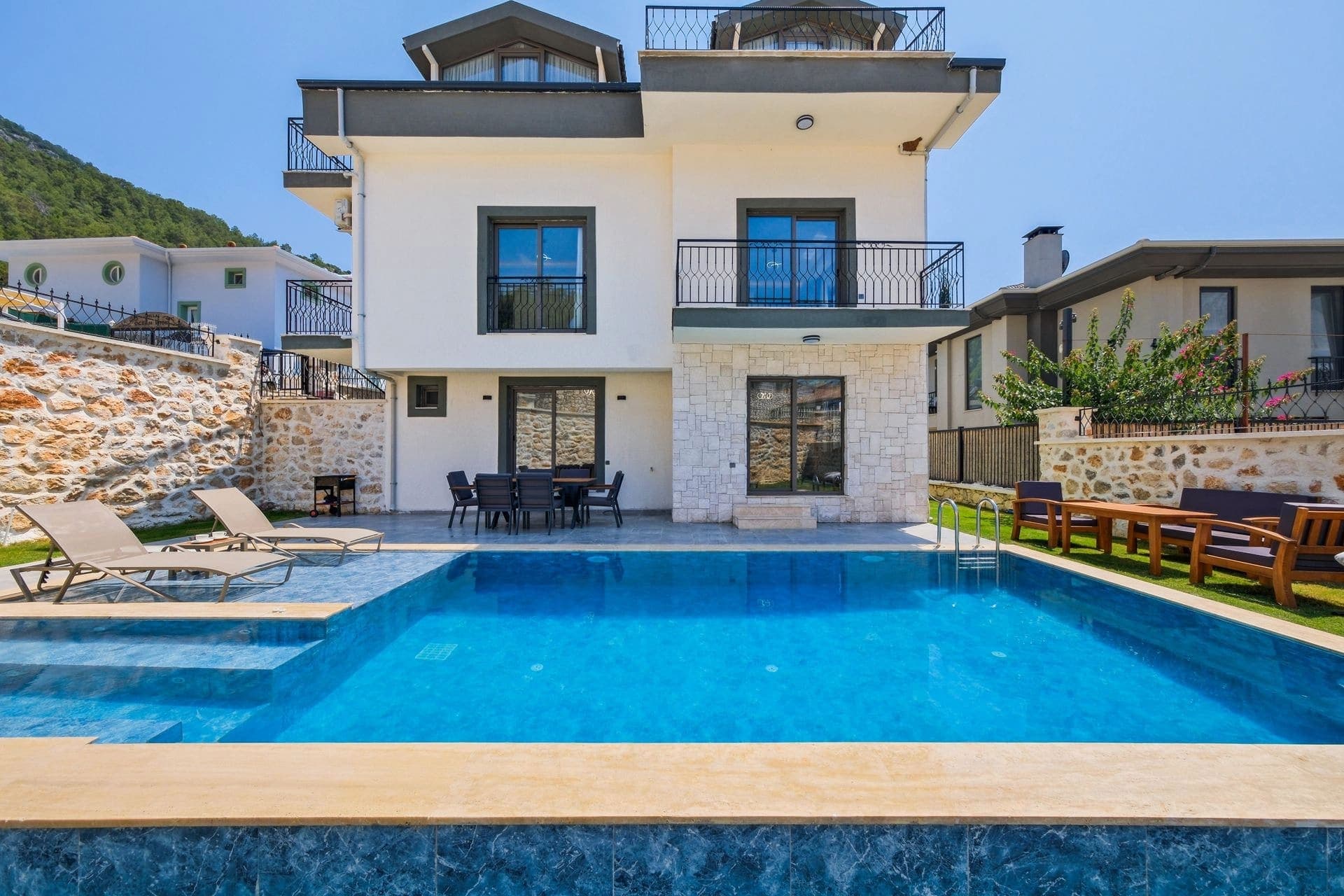 Mavi havuz ve şezlongların önünde çok katlı modern villanın dış cephesi