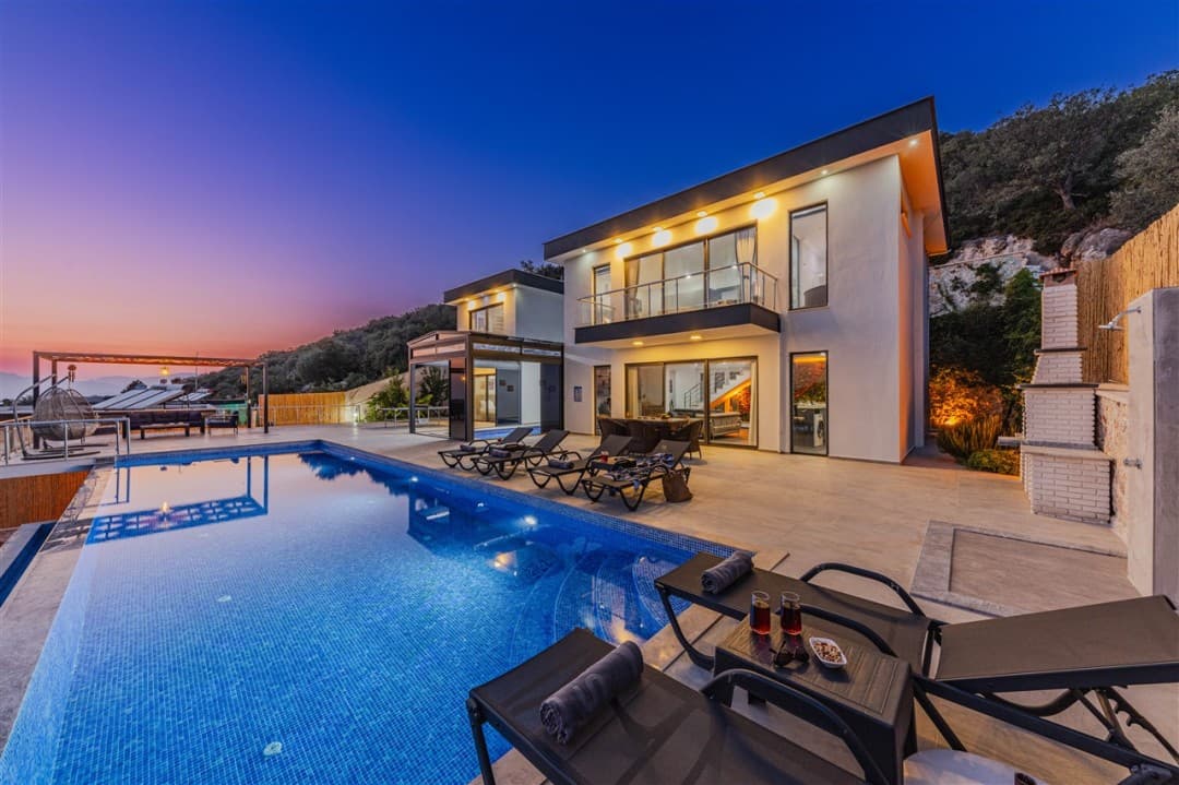 Akşam saatlerinde aydınlatmalı havuzu ve şezlongları bulunan iki katlı villa.